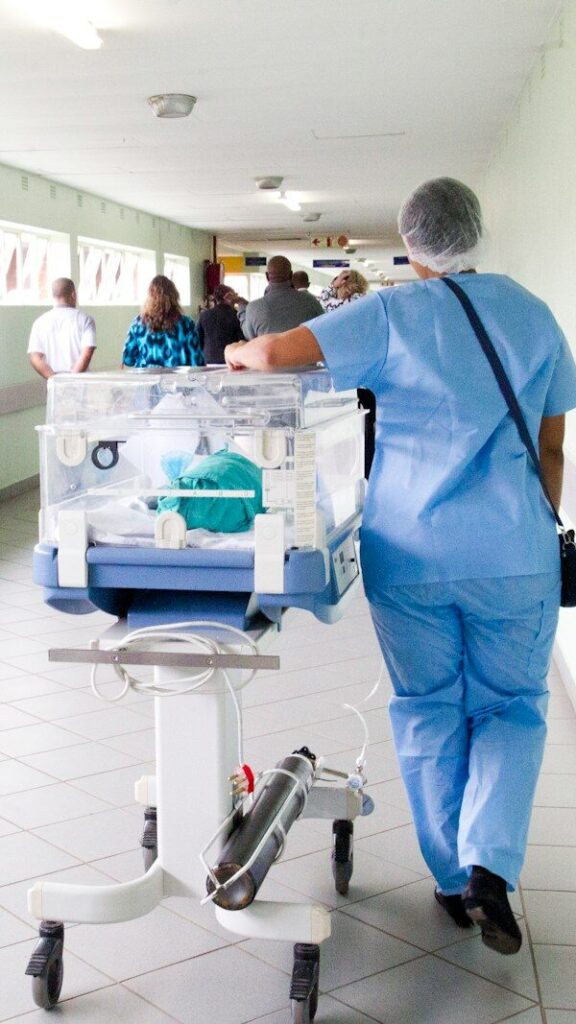 person walking on hallway in blue scrub suit near incubator